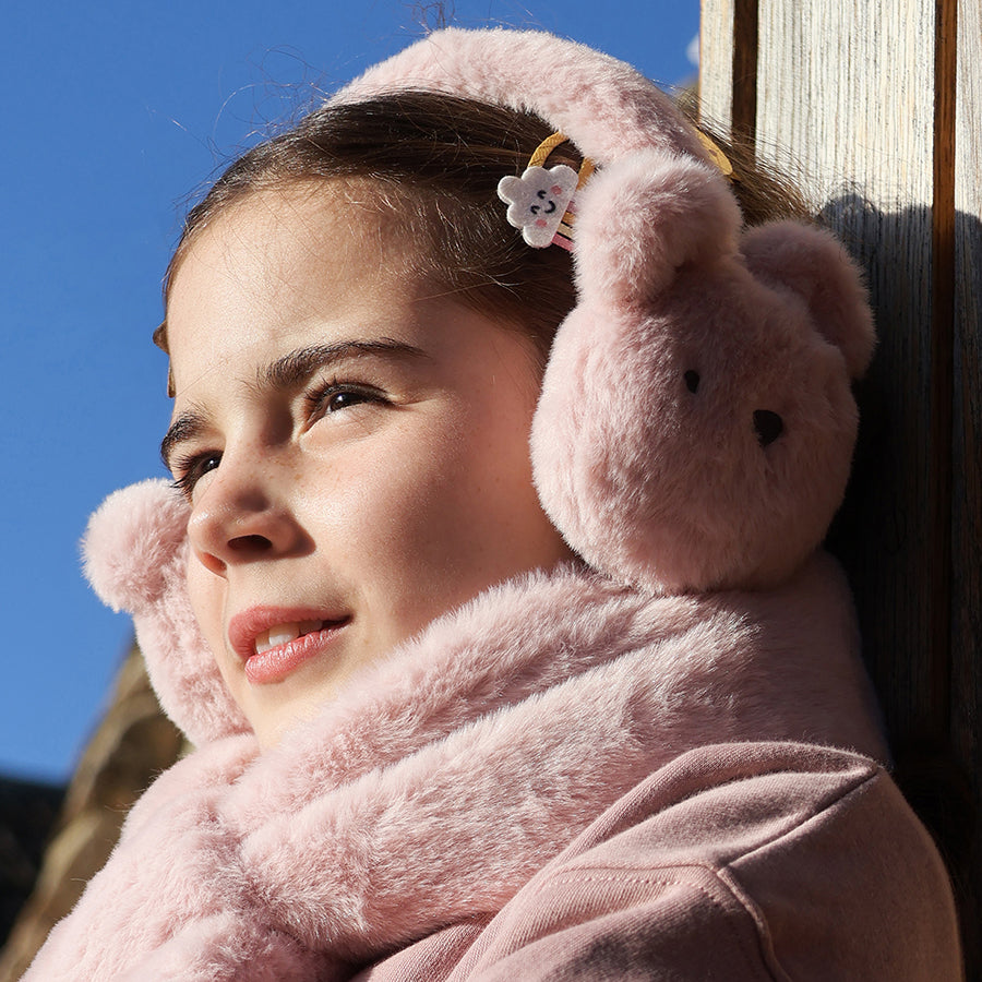 Young girl wearing pink bear-shaped earmuffs against a blue sky.